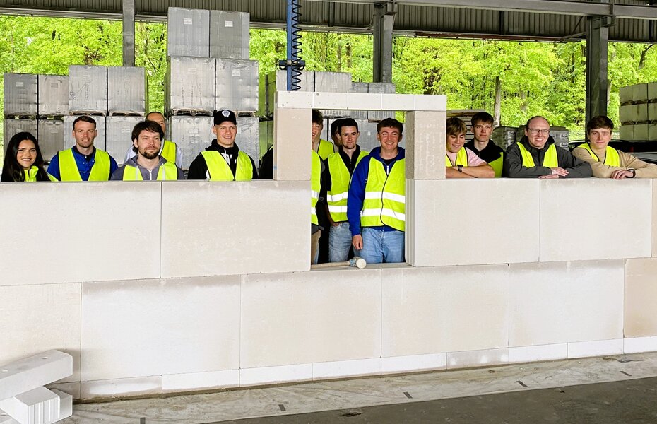 Studierende der Universität Siegen stehen hinter einer gemeinsam errichteten Mauer aus großformatigen Mauerwerkselementen.