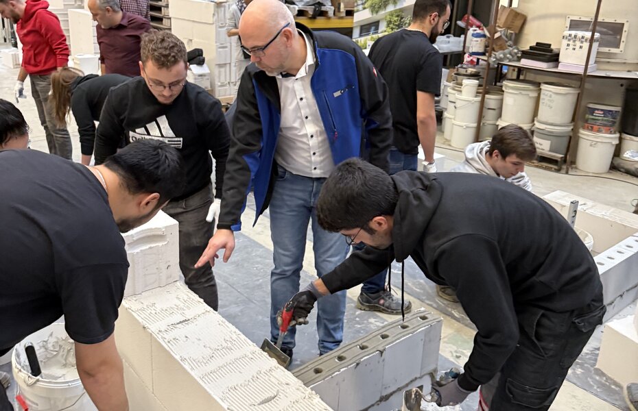 Maurermeister weist Studierende der Universität Duisburg-Essen in die praktische Ausführung von Mauerwerksarbeiten ein.